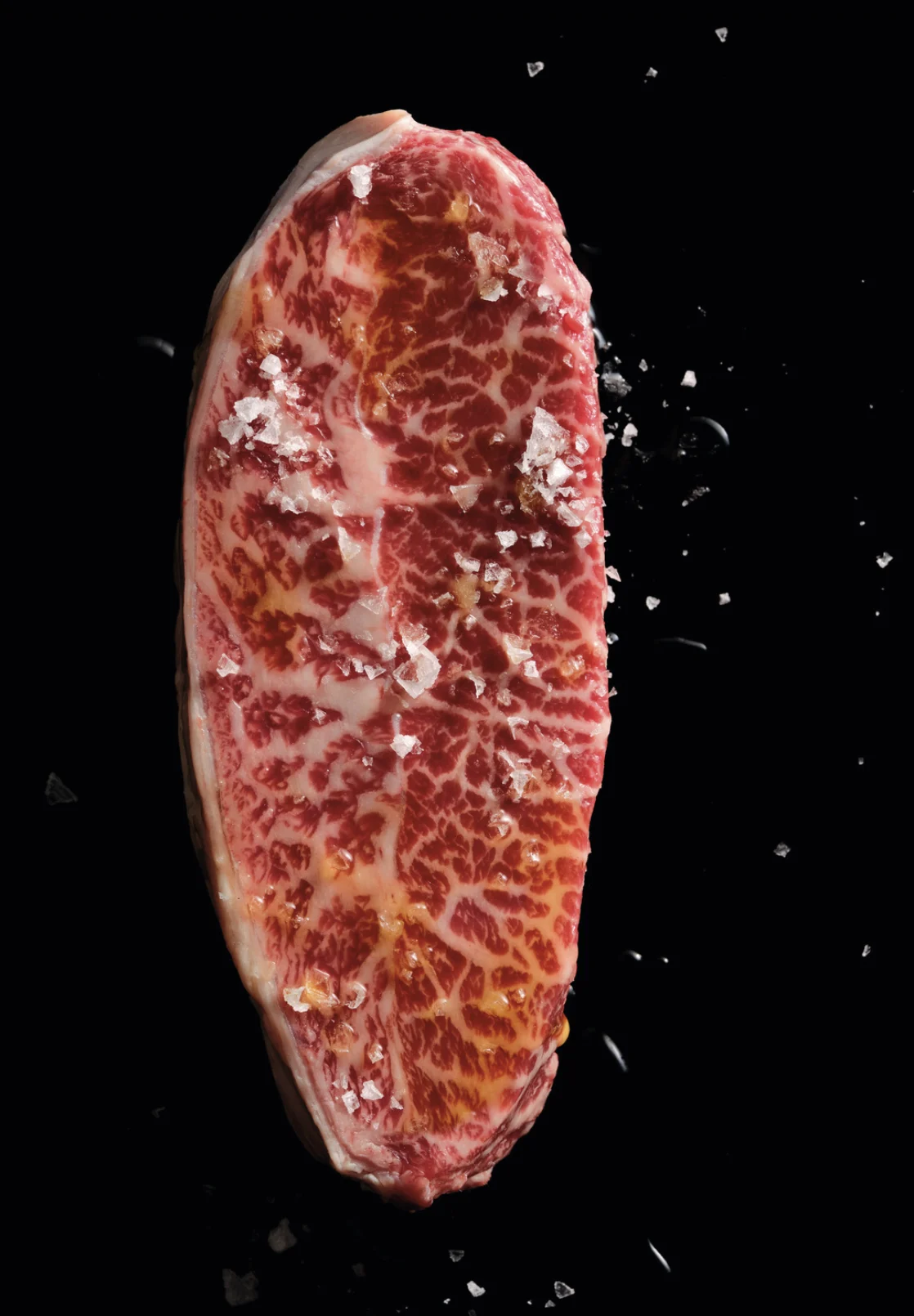 A richly marbled ICON Wagyu steak, isolated against black